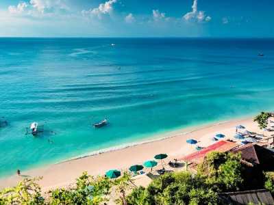 Traumhafter Sandstrand von Bali mit türkisblauem Meer, Sonnenschirmen und traditionellen Booten im Wasser.