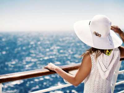 Frau mit weißem Sonnenhut genießt den Blick auf das offene Meer von einem Kreuzfahrtschiff aus.