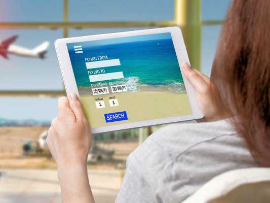 Frau hält ein Tablet mit einer Online-Flugbuchungsseite, während ein Flugzeug im Hintergrund startet.