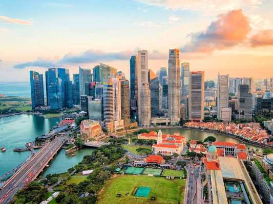 Atemberaubende Luftaufnahme der modernen Skyline von Singapur mit Wolkenkratzern, Wasserwegen und historischen Gebäuden bei Sonnenuntergang.