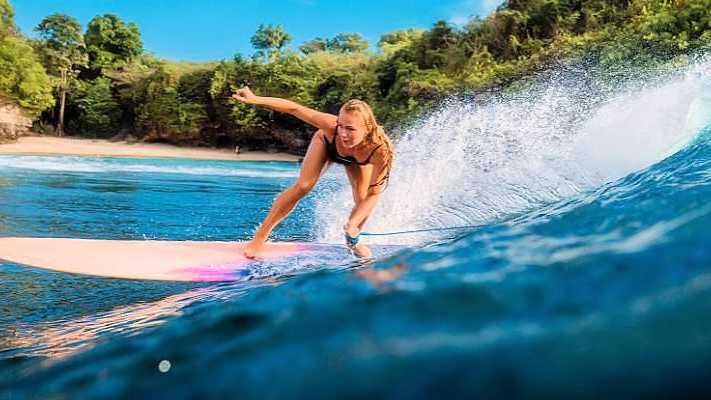 Surferin auf einer Welle an einem tropischen Strand auf Bali, umgeben von kristallklarem Wasser und grüner Natur