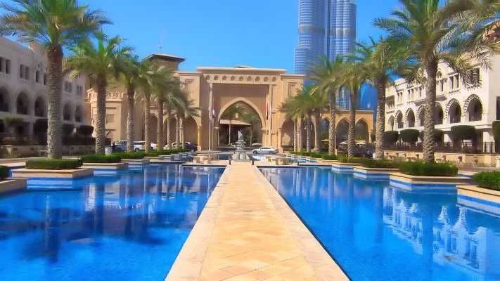 Luxuriöse Architektur in Dubai mit beeindruckendem Eingangstor, Palmen gesäumtem Wasserbecken und moderner Skyline im Hintergrund