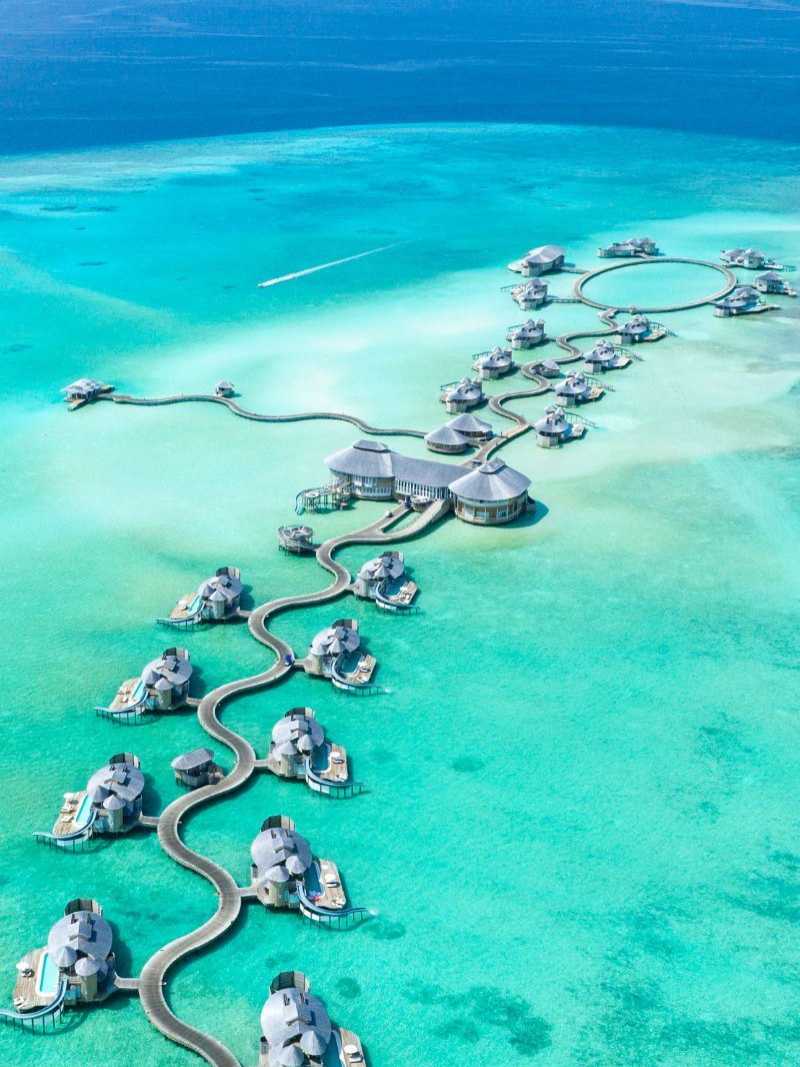 Luftaufnahme von luxuriösen Wasserbungalows auf den Malediven, verbunden durch geschwungene Holzstege über türkisfarbenem Wasser