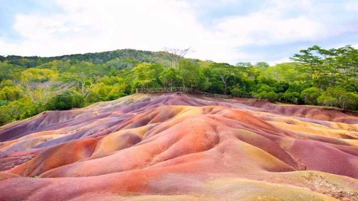 Farbenfrohe Landschaft der Siebenfarbigen Erde auf Mauritius, umgeben von grünen tropischen Wäldern und einem klaren Himmel.