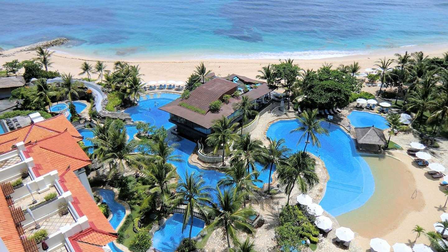 Luxusresort auf Bali mit tropischer Poollandschaft, Palmen und direktem Zugang zum Sandstrand