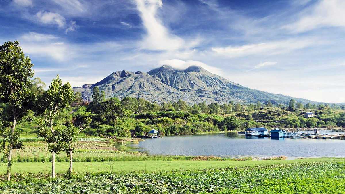 Mount Batur auf Bali mit grünen Feldern, einem See und klarer, blauer Himmel im Hintergrund
